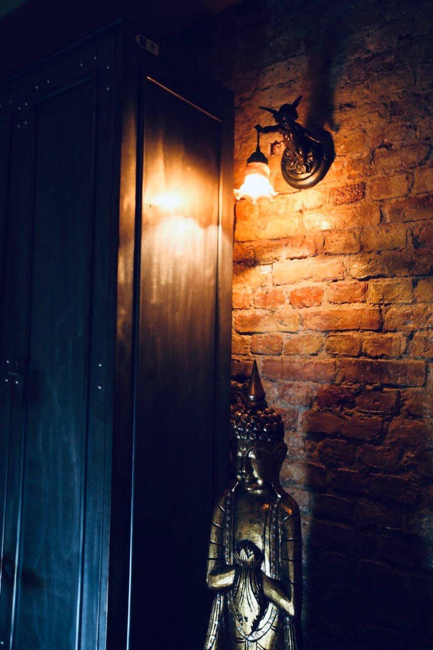 A golden Buddha statue under a wall lamp against bare brick