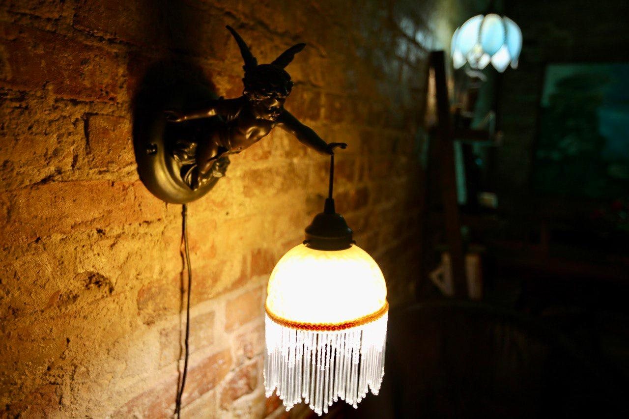 A cherub wall lamp with a beaded glass shade against bare brick